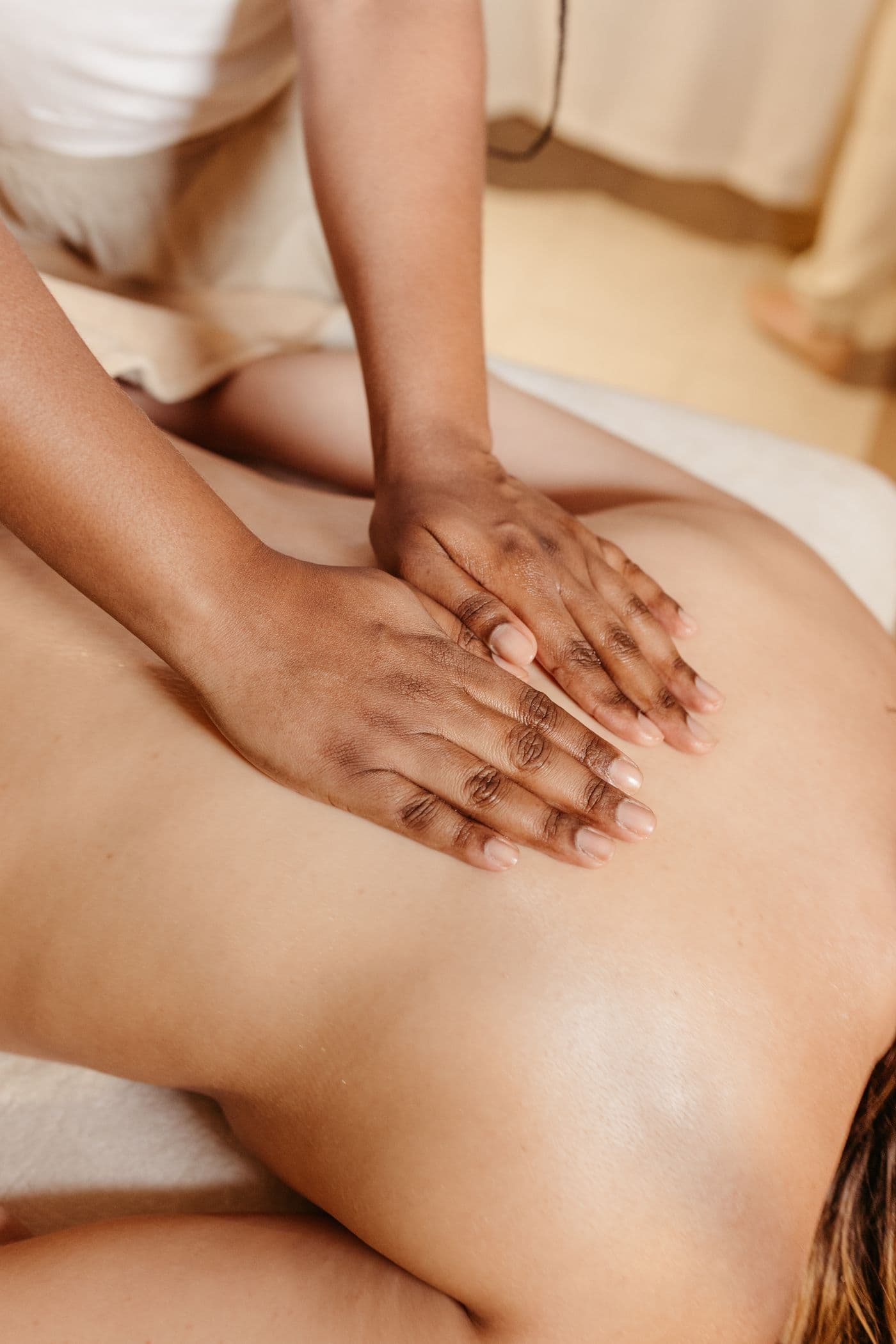 A massage therapist's hands working along a client's upper back