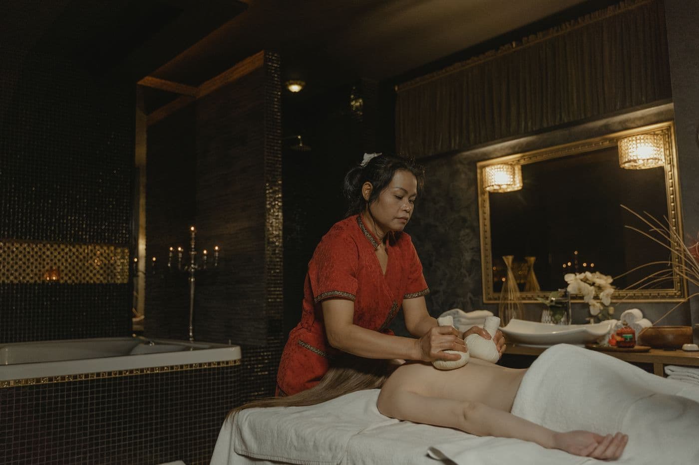 A therapist working at a candlelit massage table in a warm, quiet spa room